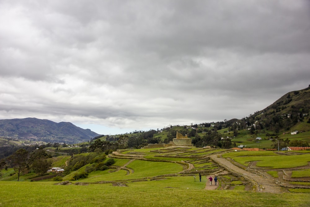 green grass field near green mountains under white clouds during daytime