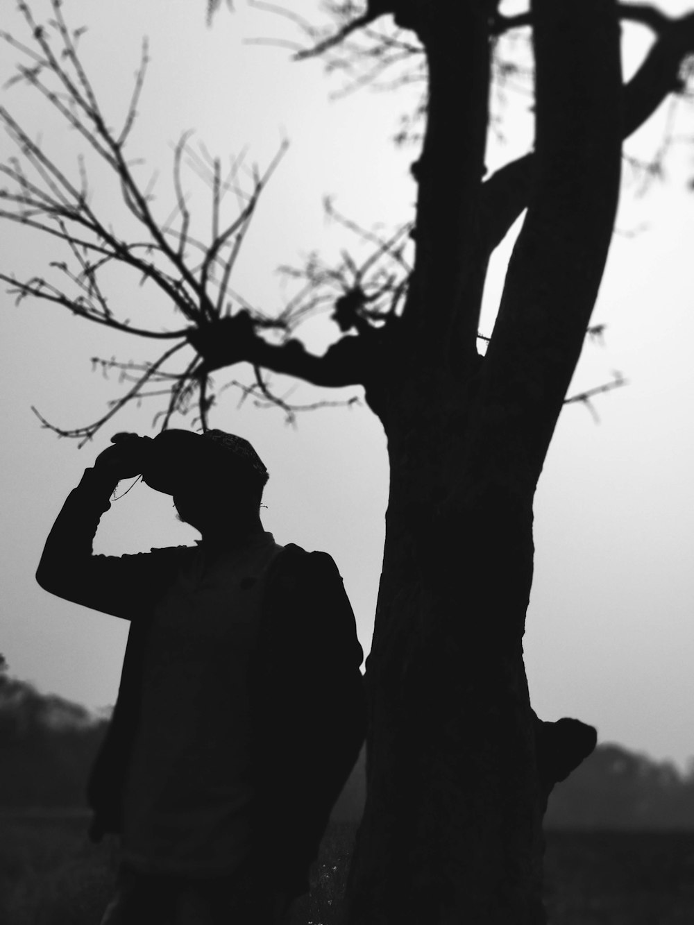 silhouette of man standing beside bare tree during daytime