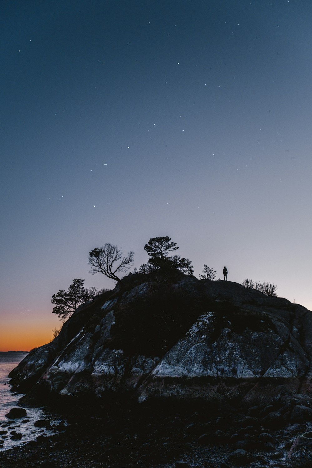 silhouette of 2 people standing on rock formation during night time