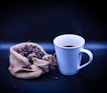 A steaming cup of coffee on a white table with a dark teal napkin and a black coffee bag in the background.