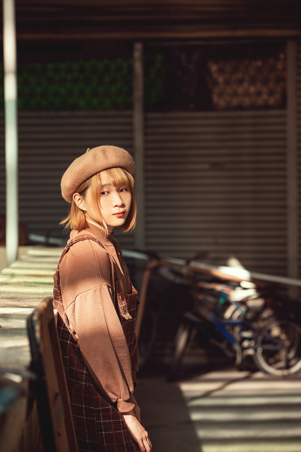 woman in brown leather jacket and brown fedora hat standing near black motorcycle during daytime