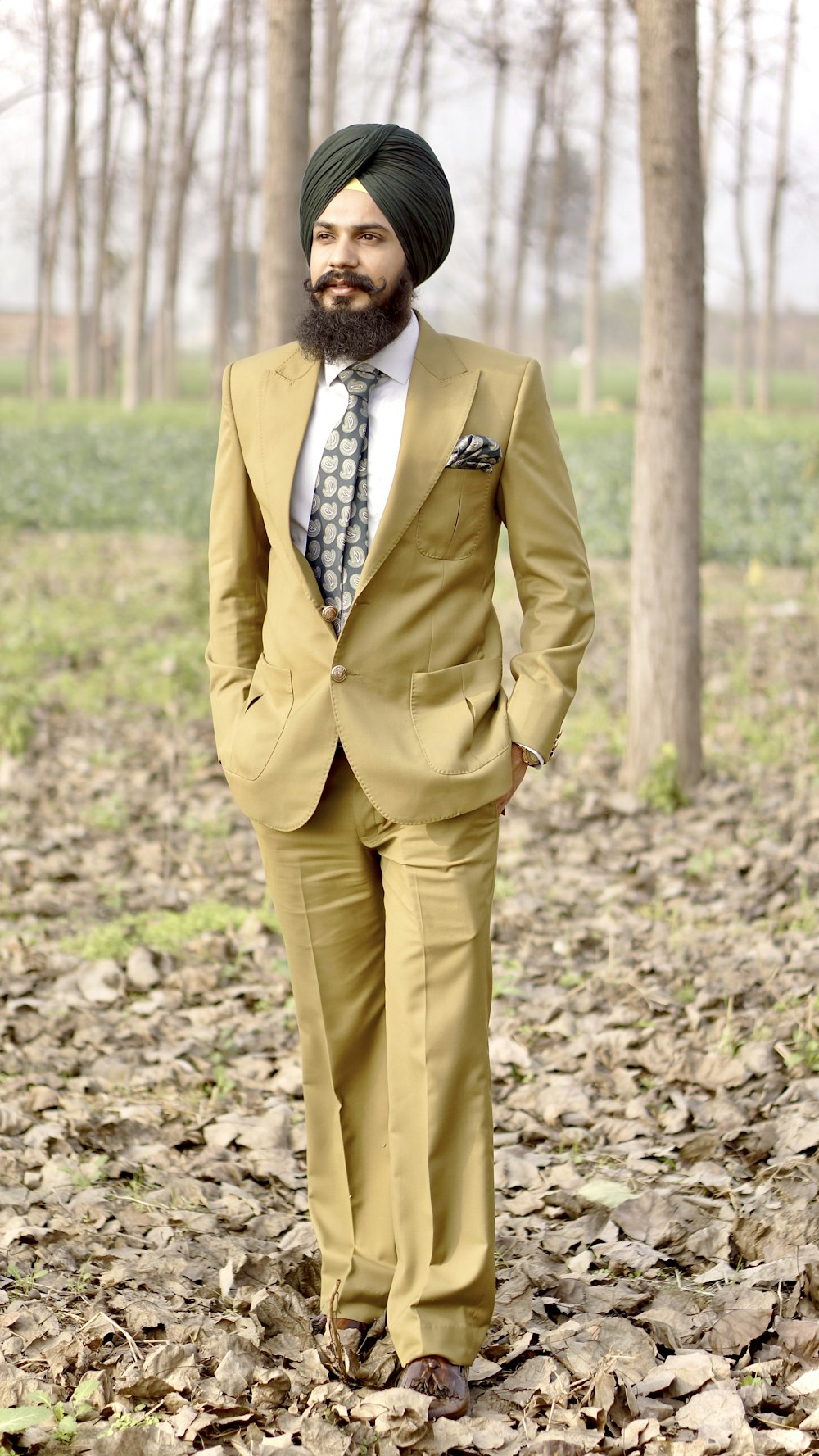 man in brown suit jacket and brown pants standing on brown dried leaves during daytime