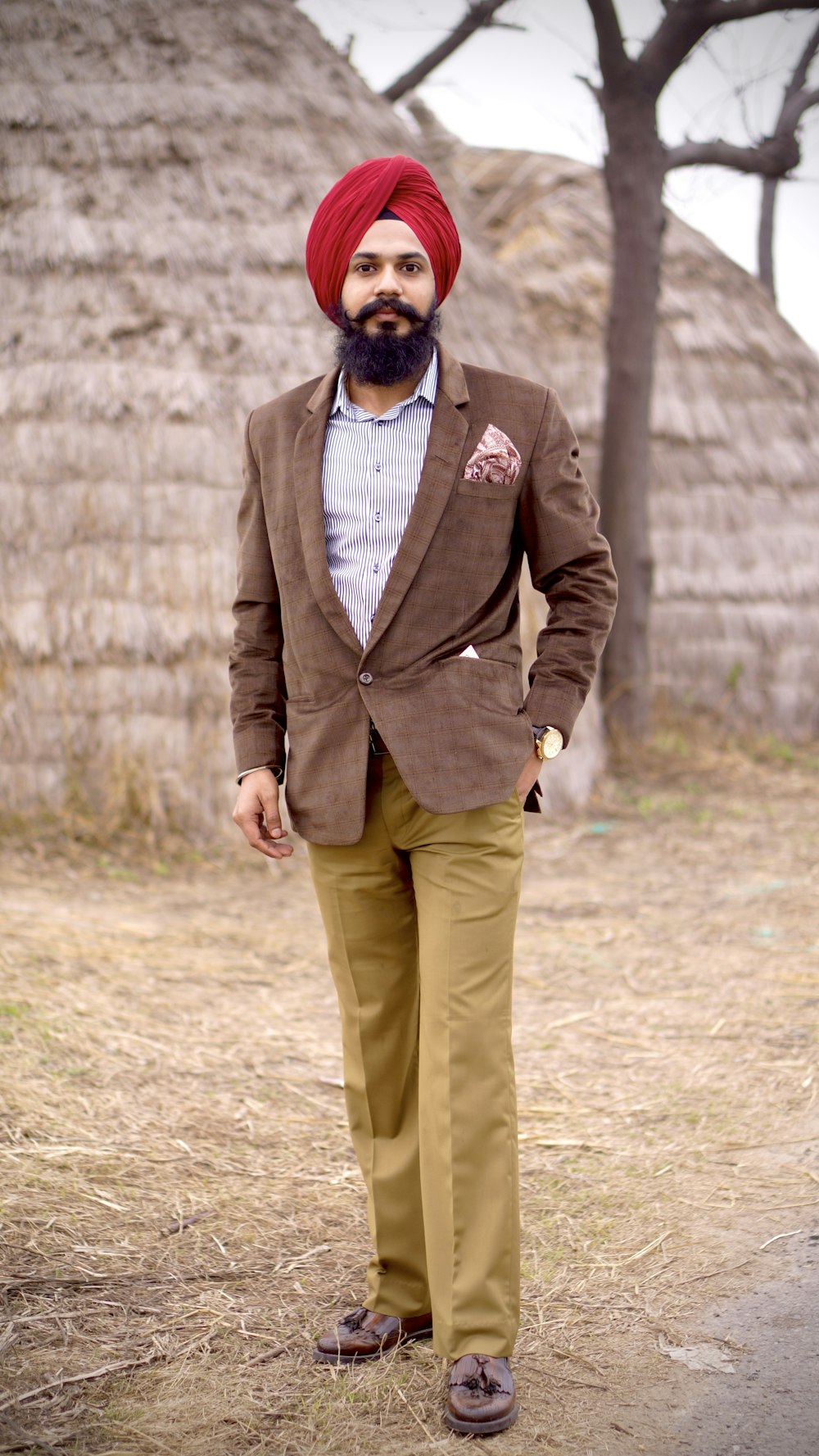 uomo in cappotto marrone e pantaloni beige in piedi sul campo marrone durante il giorno