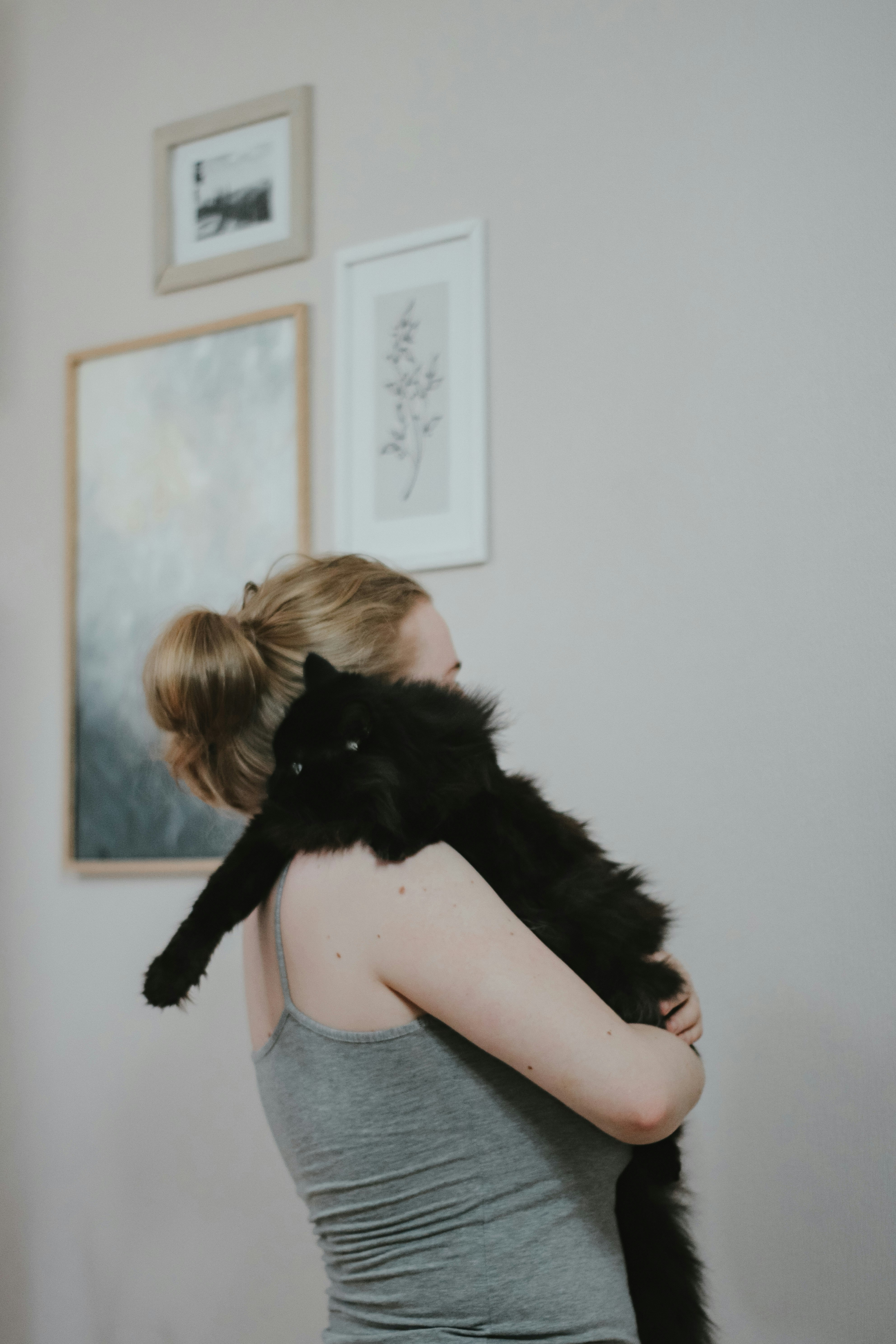 woman in gray tank top hugging black cat