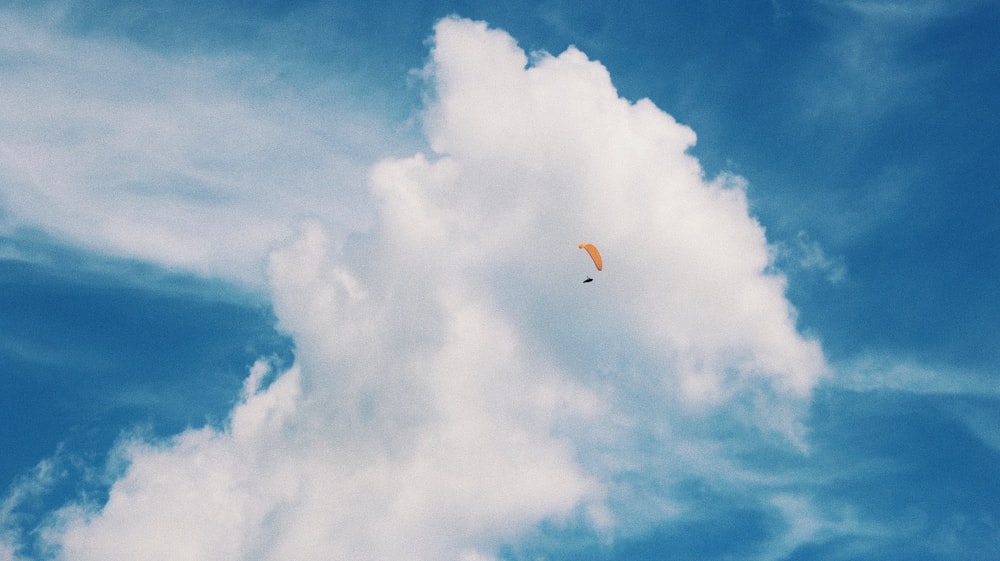 昼間の白い雲と青い空の下でオレンジ色のパラシュートに乗った人