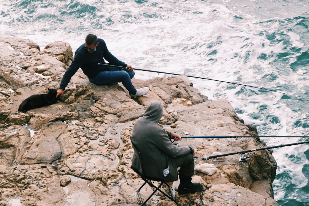 man in black jacket and black pants sitting on rock near body of water during daytime