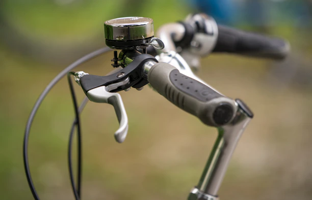 Close-up of a colorful bicycle handlebar with a bell and brake levers in bright sunlight.
