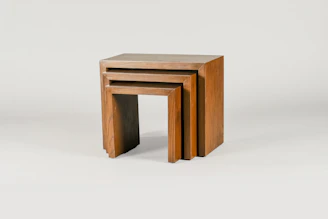 Three wooden nesting tables are arranged one inside the other. They are rectangular with a simple and minimalist design, showcasing a natural wood finish with visible grain patterns.