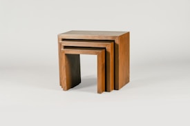 Three wooden nesting tables are arranged one inside the other. They are rectangular with a simple and minimalist design, showcasing a natural wood finish with visible grain patterns.