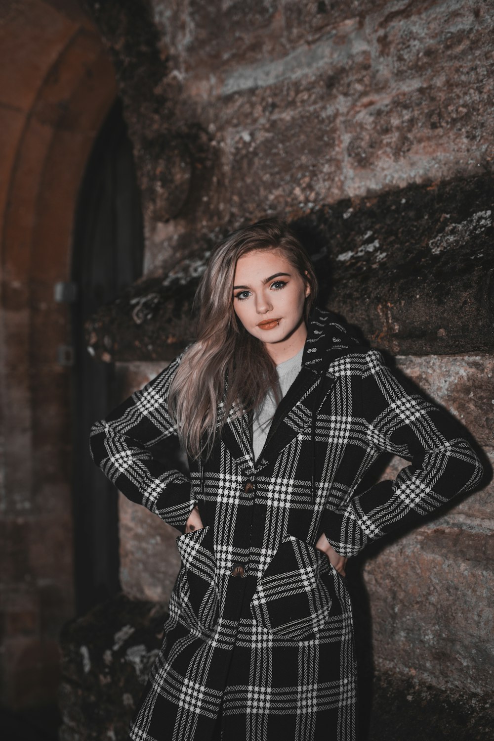 woman in black and white checkered coat standing beside brown brick wall