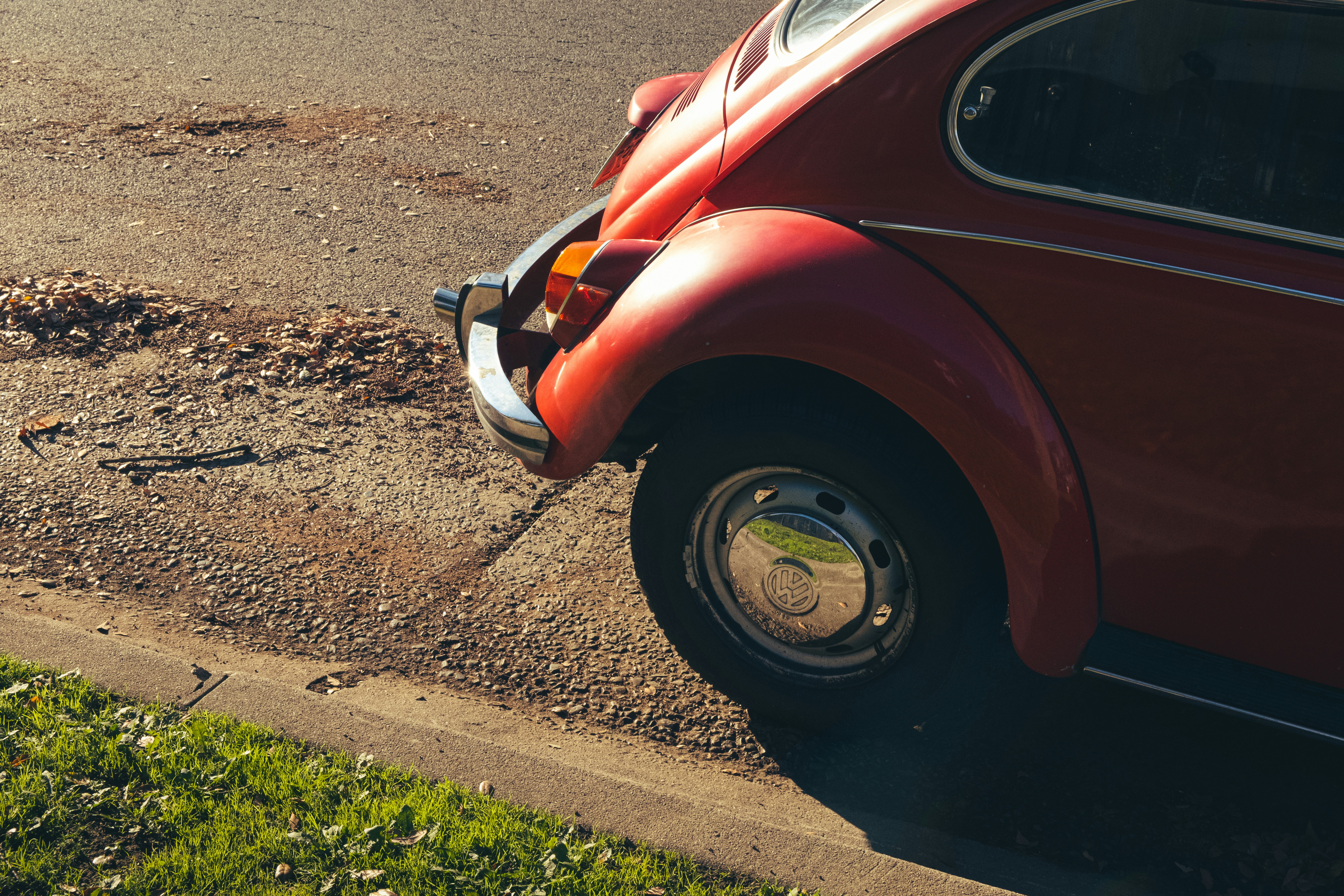 A vintage Volkswagen Beetle parked on a scenic road with sunlight highlighting its curves.