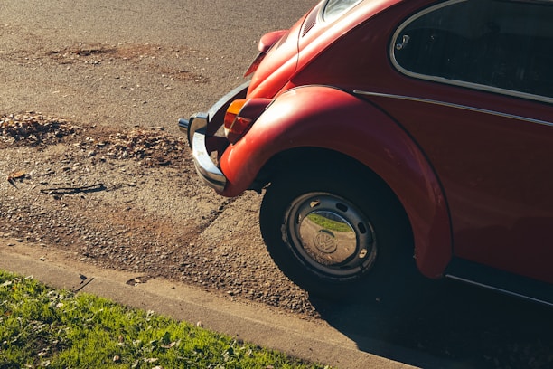 A sleek Volkswagen Beetle parked by a sunlit coastal road, captured in minimalist style.