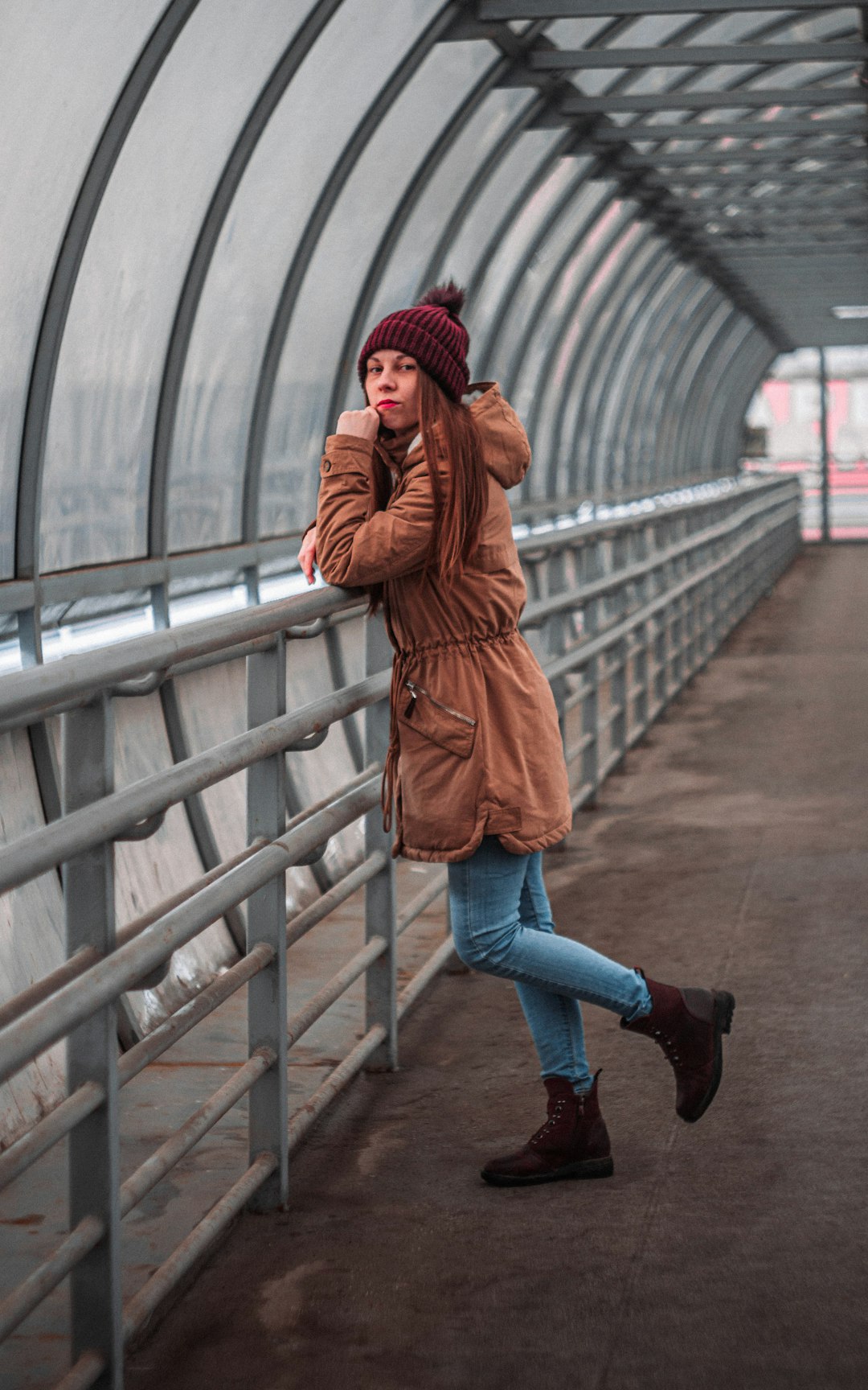 woman in brown coat and blue denim jeans walking on bridge
