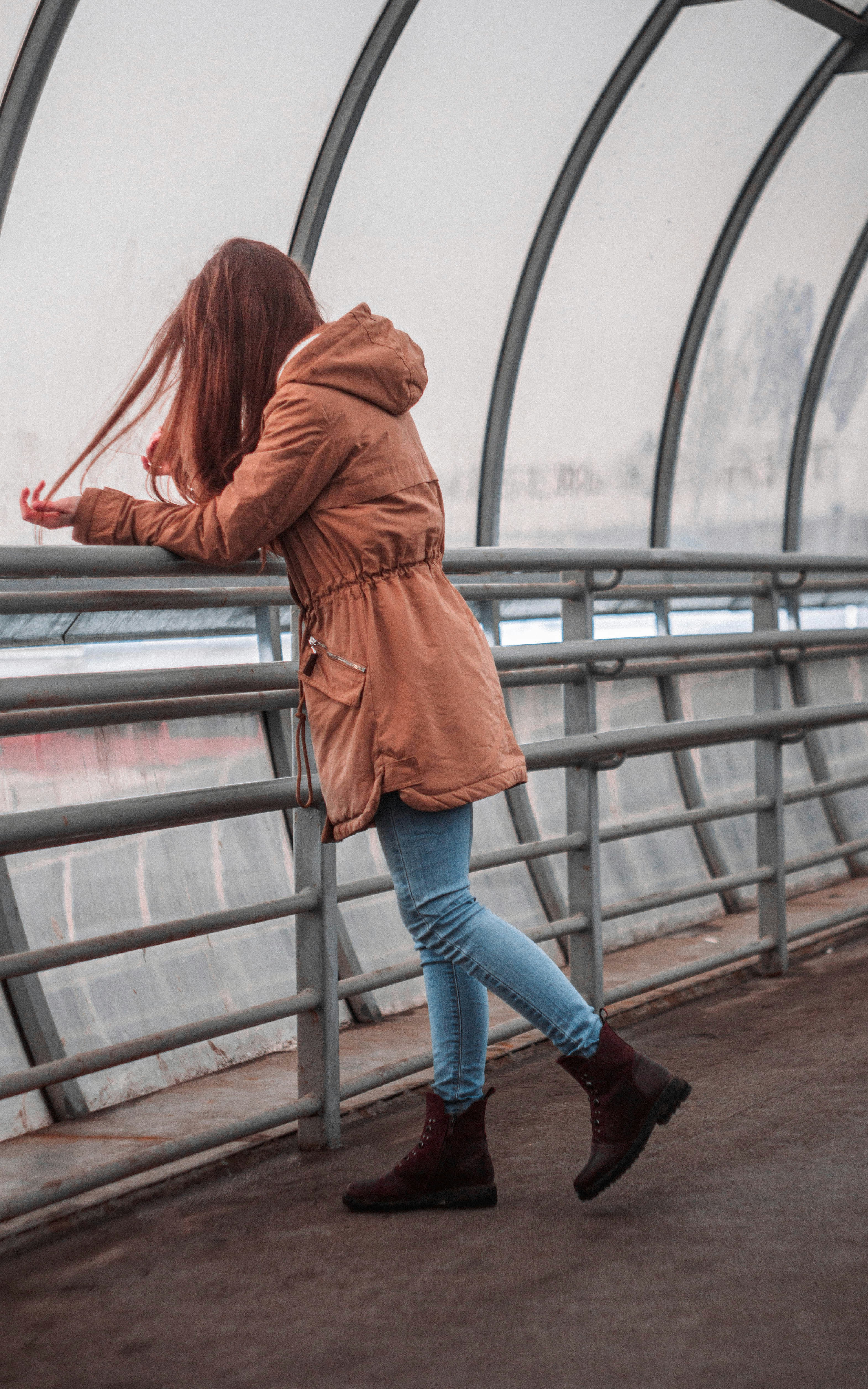 woman in brown coat and blue denim jeans standing on gray staircase