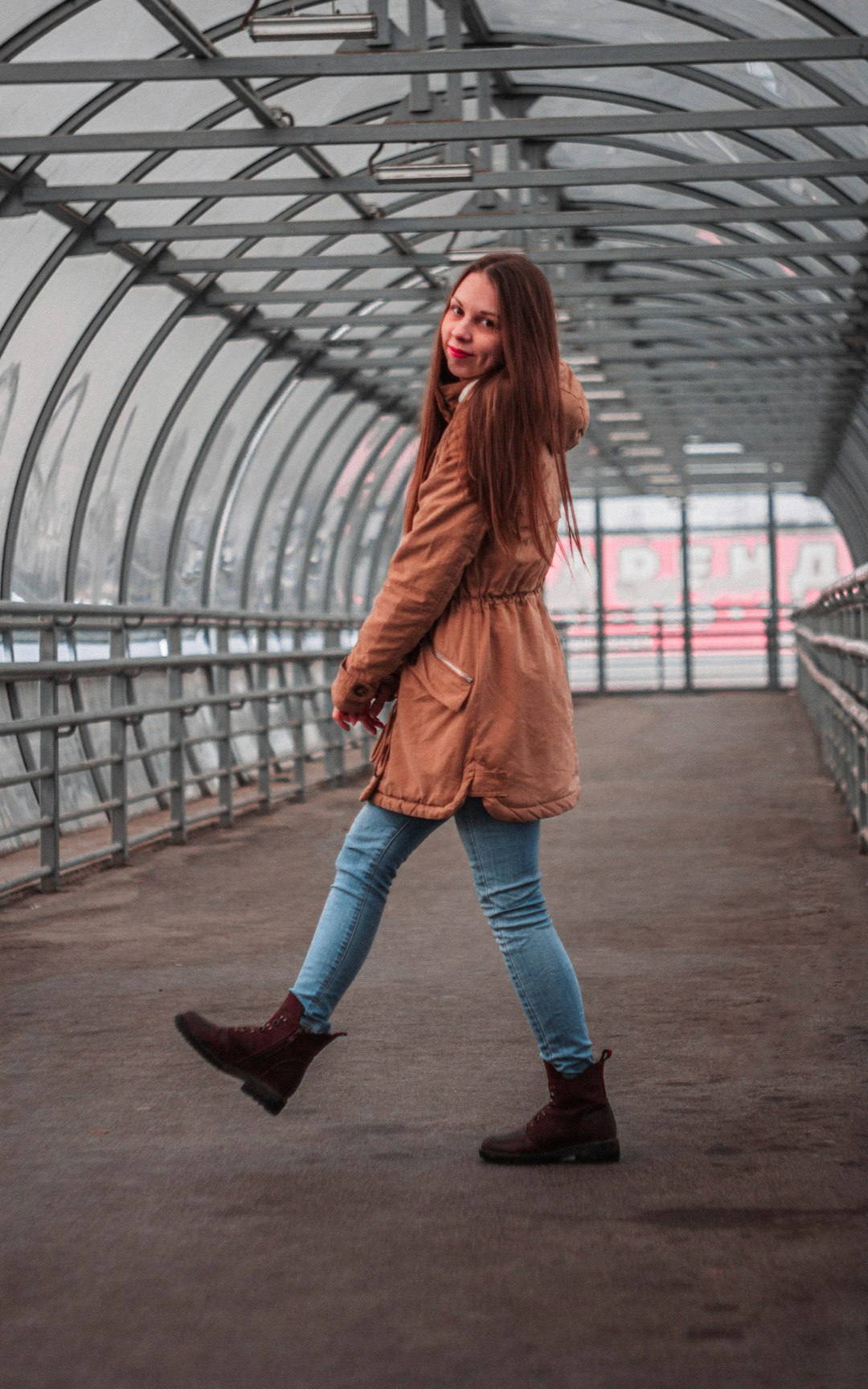 woman in brown coat and blue denim jeans standing on bridge