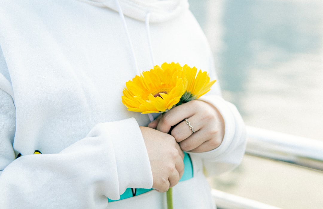 person in white hoodie holding yellow flower