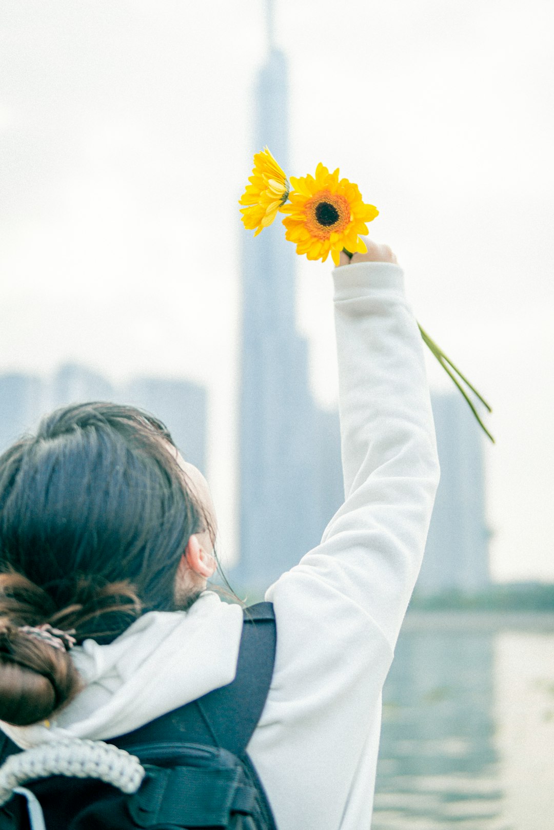 woman in white long sleeve shirt holding sunflower during daytime