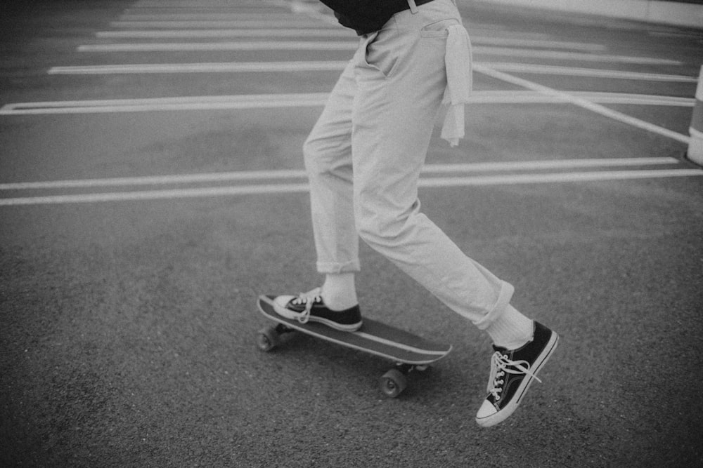 man in black hoodie and white pants standing on skateboard in grayscale photography