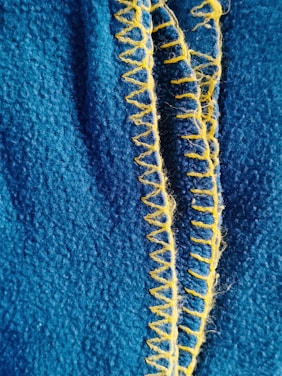 A close-up view of textured blue fabric with bright yellow zigzag stitching running down the center.