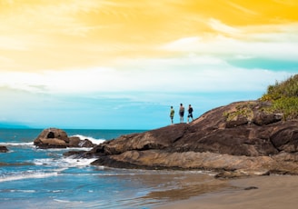 2 person standing on brown rock formation near body of water during daytime