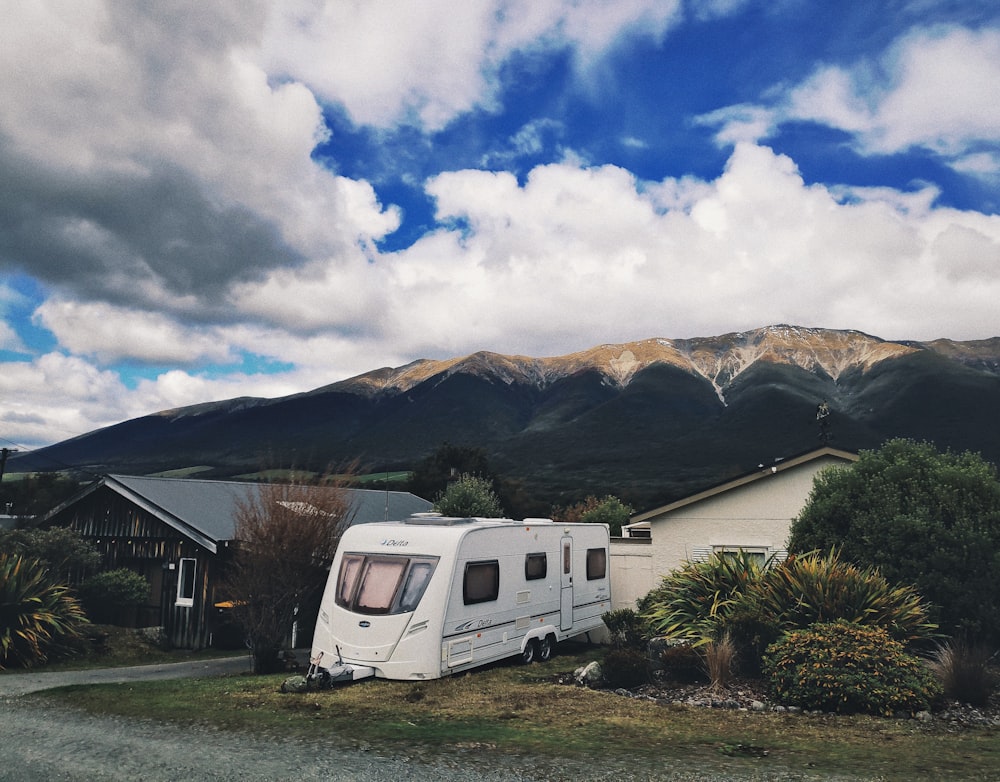 white van near green grass field and mountain under white clouds and blue sky during daytime