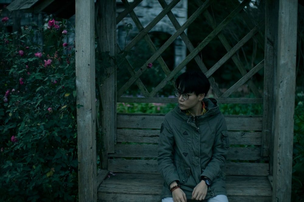 man in gray jacket sitting on wooden bridge