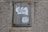 A worn and rusted metal sign is mounted on a textured concrete wall. The sign displays partially torn white paper with the word 'Mind' prominently visible, suggesting some worn-out message.