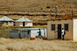 man in blue shirt and black pants standing beside white and brown house during daytime