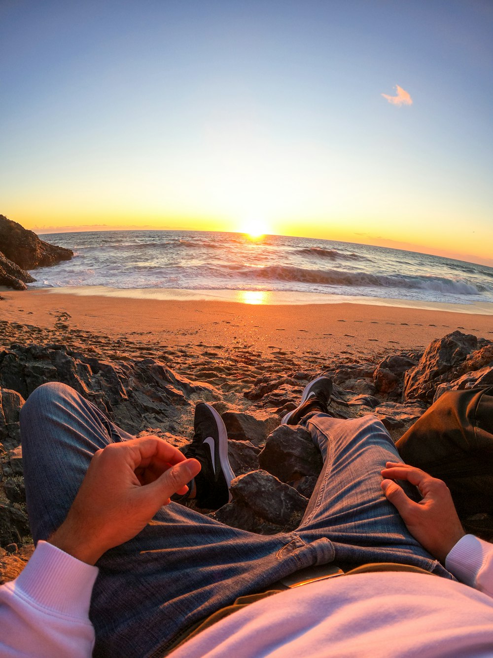 pessoa em jeans azuis sentados na rocha perto do mar durante o pôr do sol