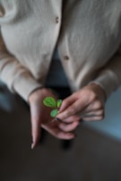 person in white blazer holding green heart ornament
