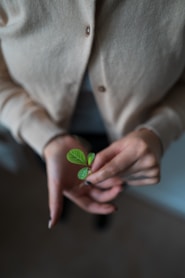person in white blazer holding green heart ornament
