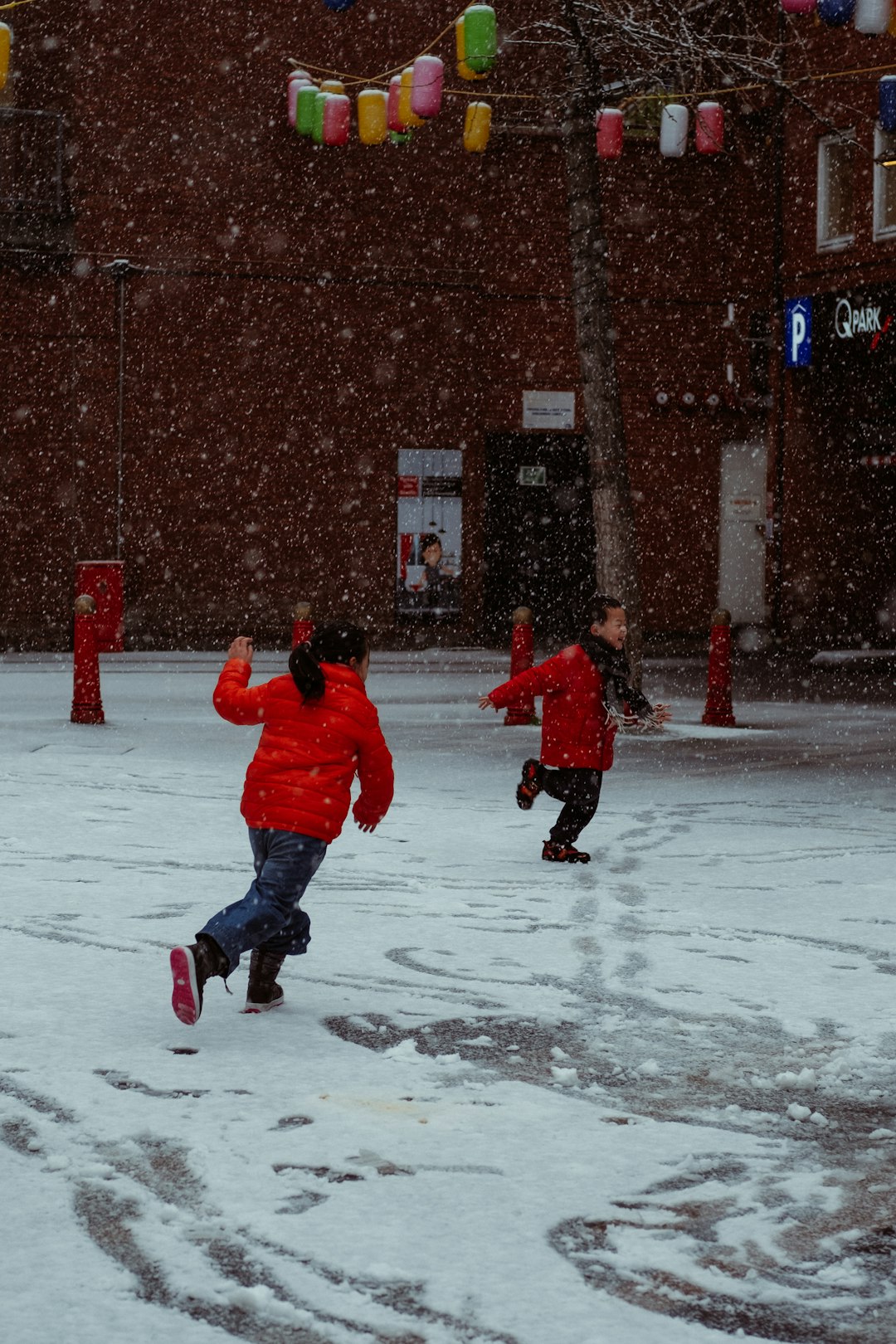 child in red jacket and blue pants walking on snow covered ground during daytime