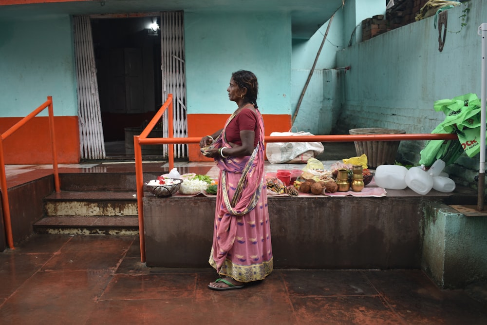 Donna in vestito rosa e bianco in piedi vicino alla bancarella del cibo