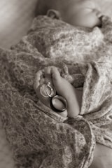 A newborn baby wrapped in a floral-patterned fabric, with their tiny feet adorned with two rings, one with a diamond stone.
