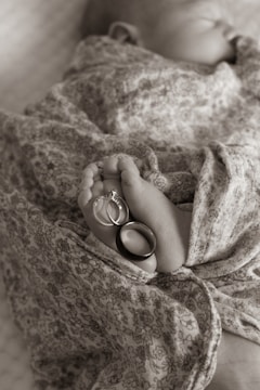 A newborn baby wrapped in a floral-patterned fabric, with their tiny feet adorned with two rings, one with a diamond stone.