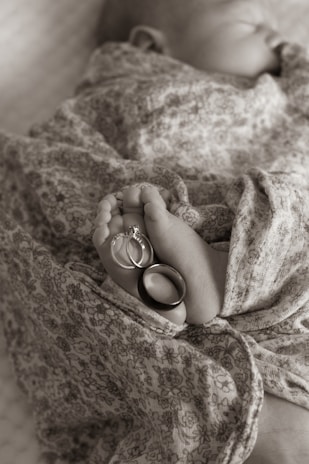 A newborn baby wrapped in a floral-patterned fabric, with their tiny feet adorned with two rings, one with a diamond stone.