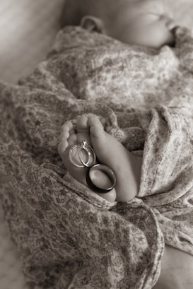 A newborn baby wrapped in a floral-patterned fabric, with their tiny feet adorned with two rings, one with a diamond stone.