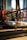 A close-up of a 3D printer in action, focusing on the extruder head as it moves over the print bed. The background is blurred, highlighting the precision machinery and components such as gears and electric wires. The scene is well-lit, emphasizing the mechanical details of the printer.