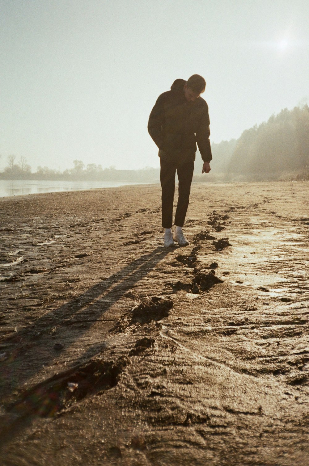 man in black jacket standing on brown sand near body of water during daytime