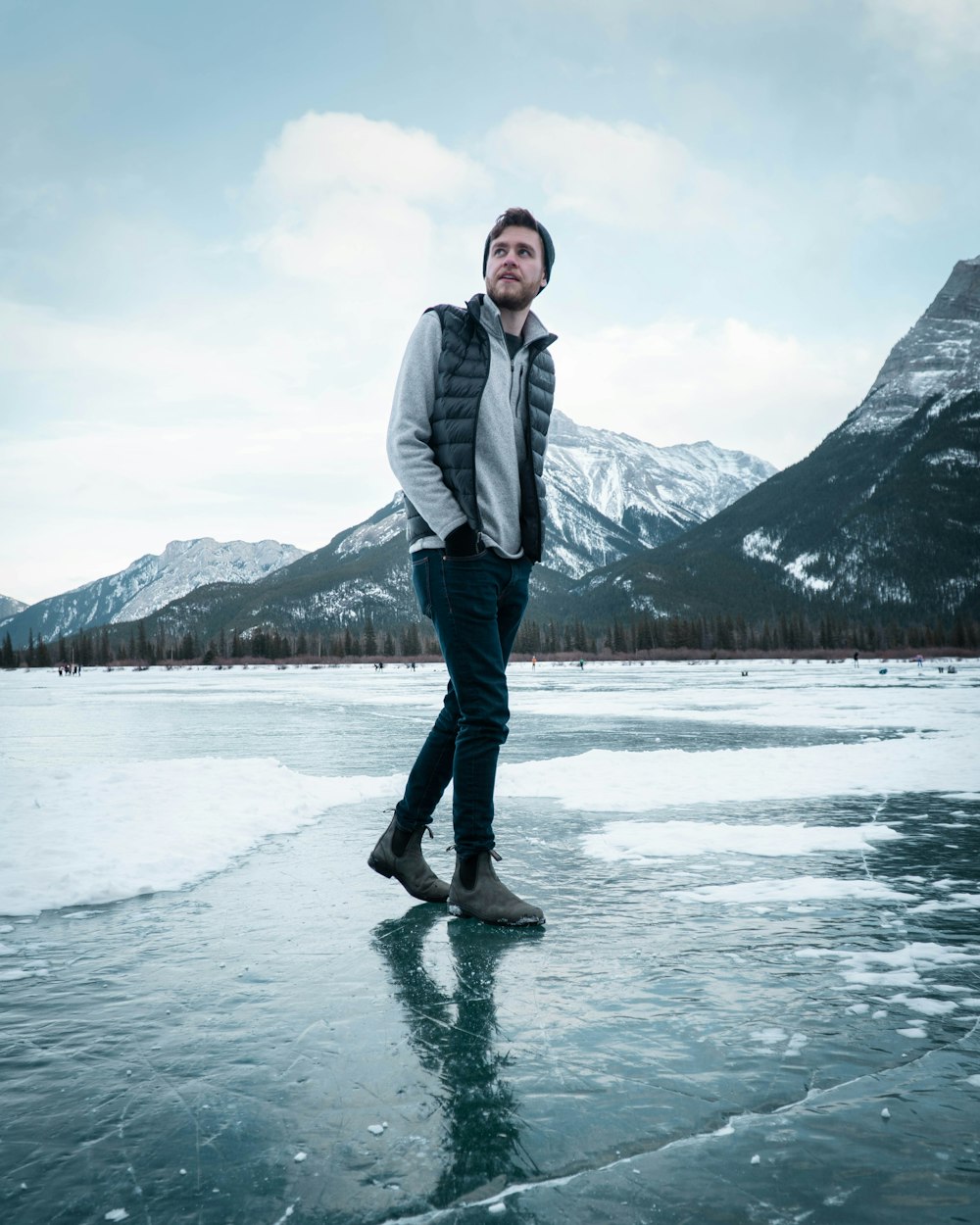 man in gray jacket standing on lake during daytime
