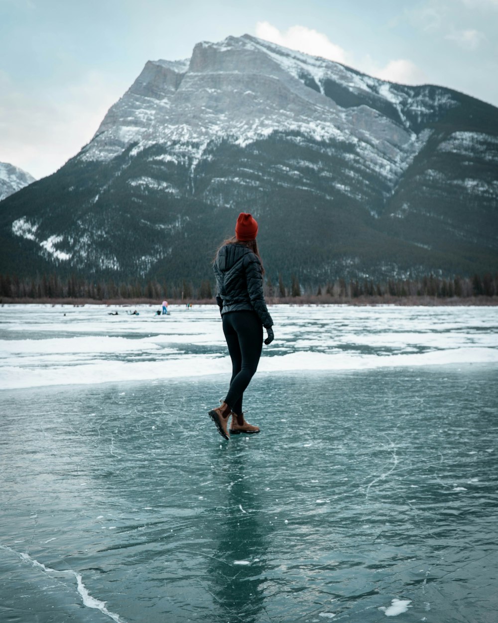 man in black jacket and black pants standing on snow covered ground near body of water