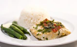 Freshly grilled coastal fish plated with rice and palm oil beans, garnished with herbs.