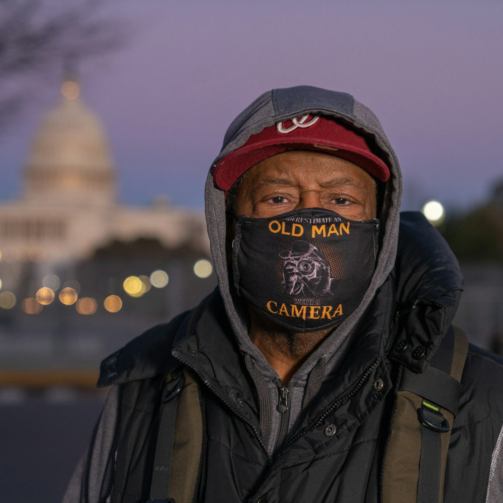 man in black leather jacket wearing red and black fitted cap