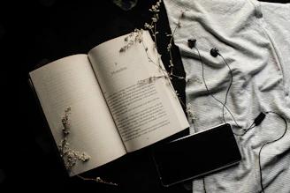 An open book beside headphones resting on a wooden table, inviting to listen.