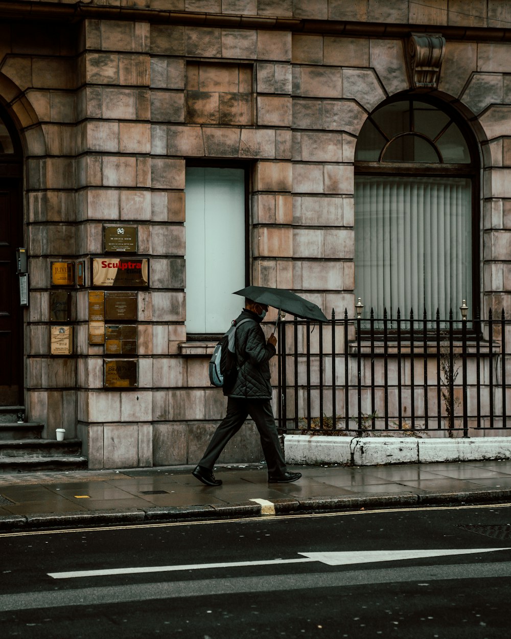 日中に歩道を歩く傘を持った黒いジャケットを着た人物