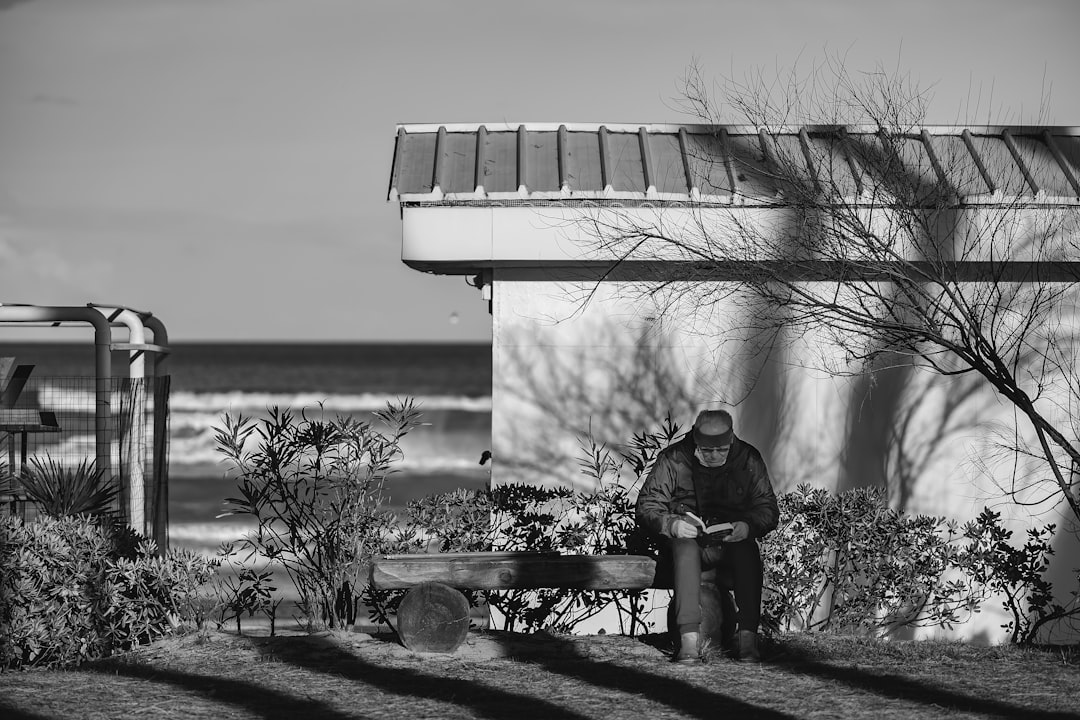 man in black jacket sitting on bench near body of water