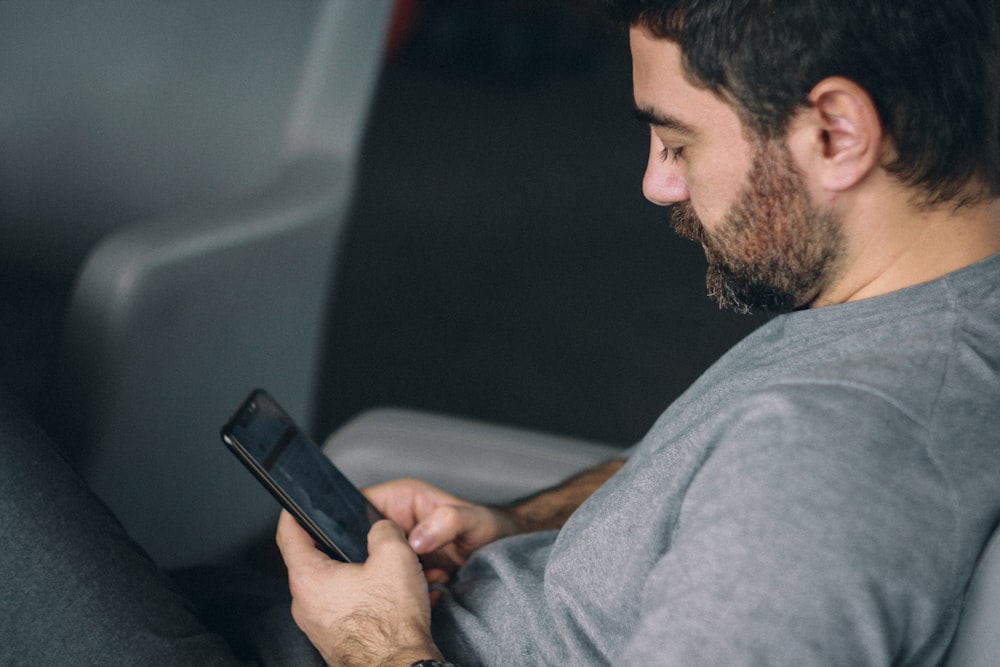 man in gray hoodie holding black smartphone