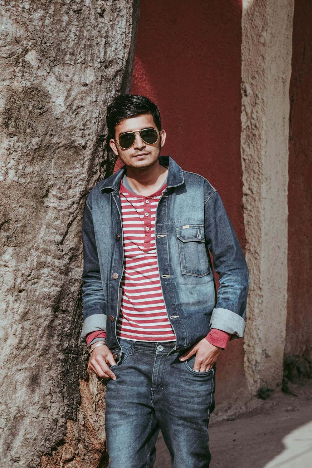 man in blue denim jacket and blue denim jeans leaning on brown concrete wall during daytime