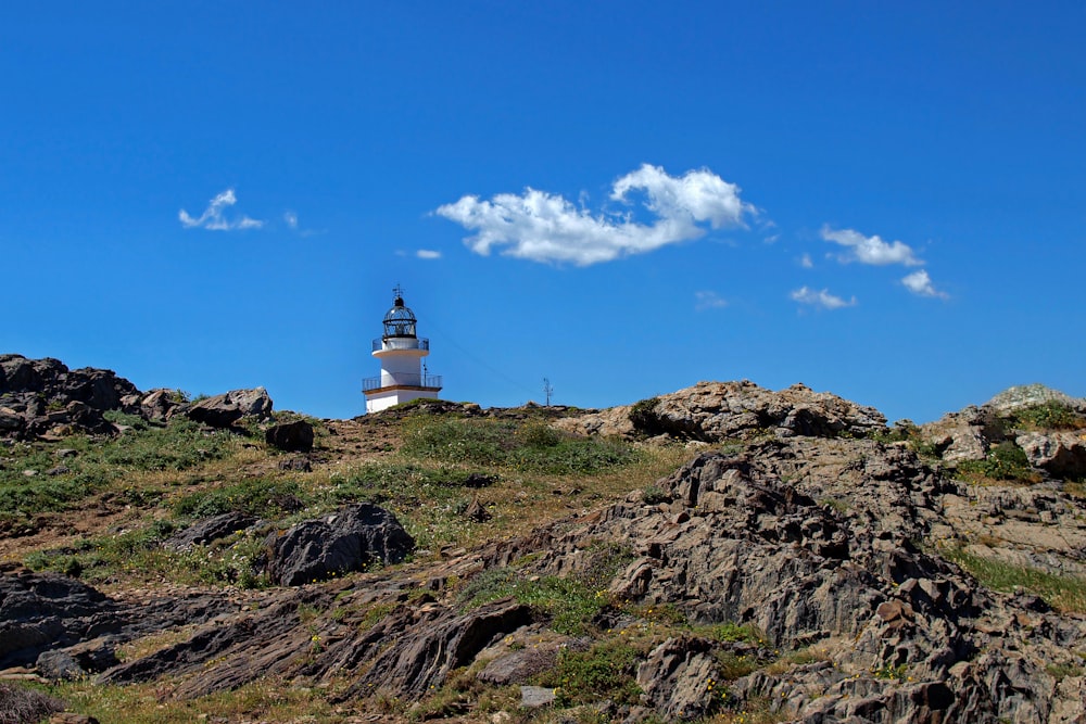 white and brown lighthouse on brown rocky mountain under blue and white sunny cloudy sky during