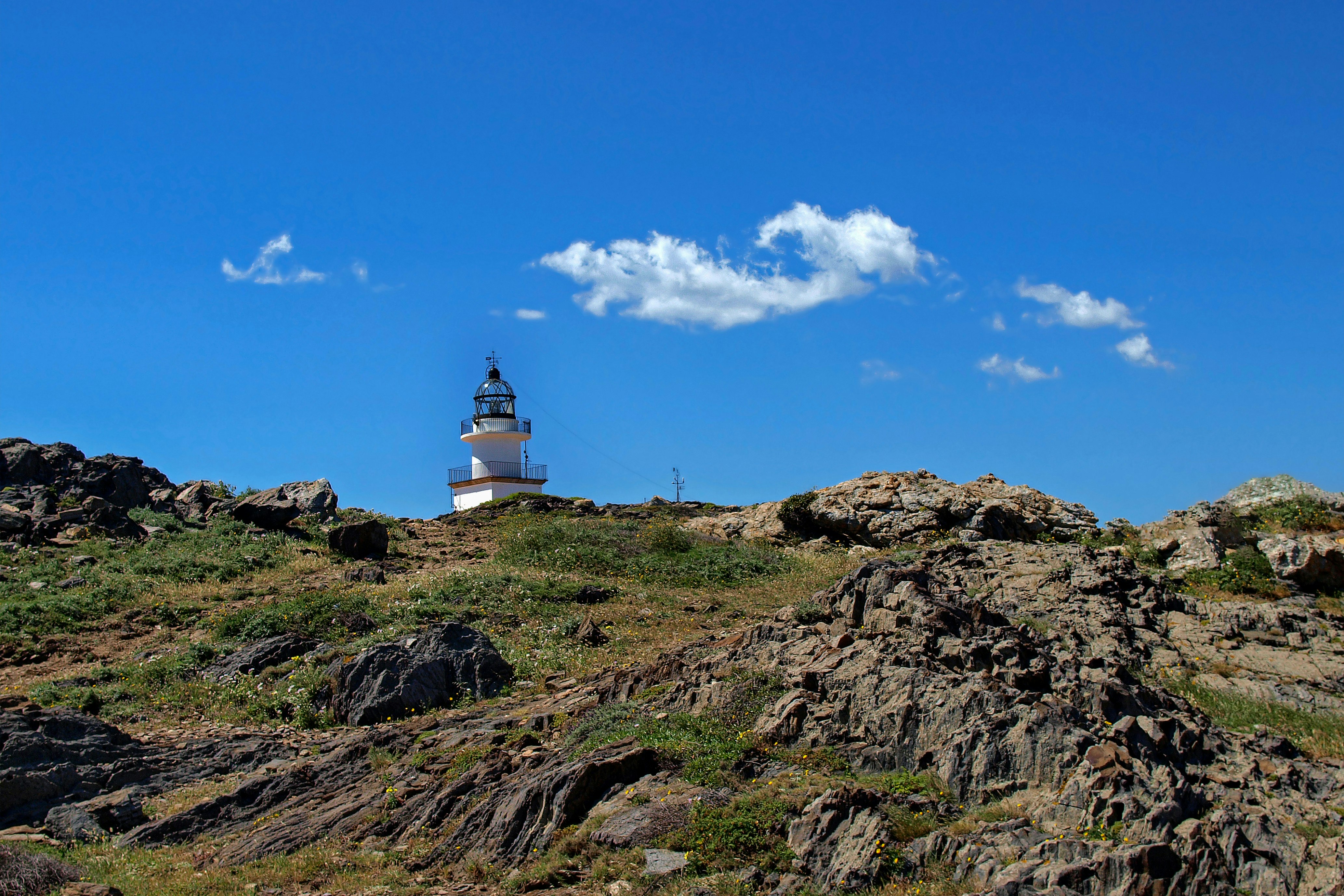 white and brown lighthouse on brown rocky mountain under blue and white sunny cloudy sky during